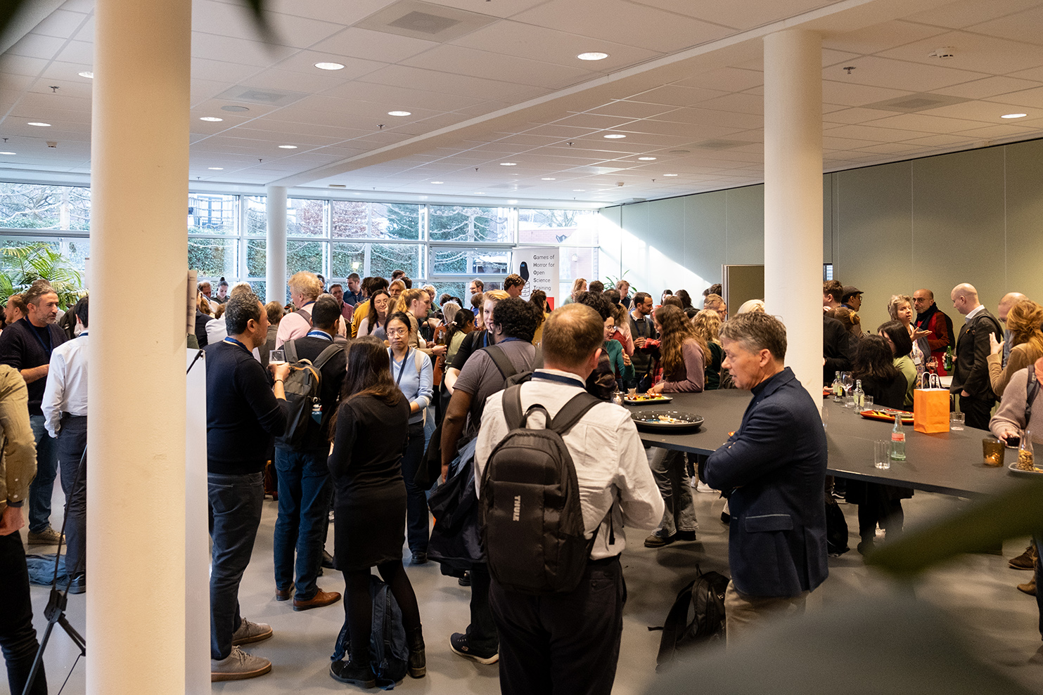 A large crowd of people standing in a foyer having drinks after the event.